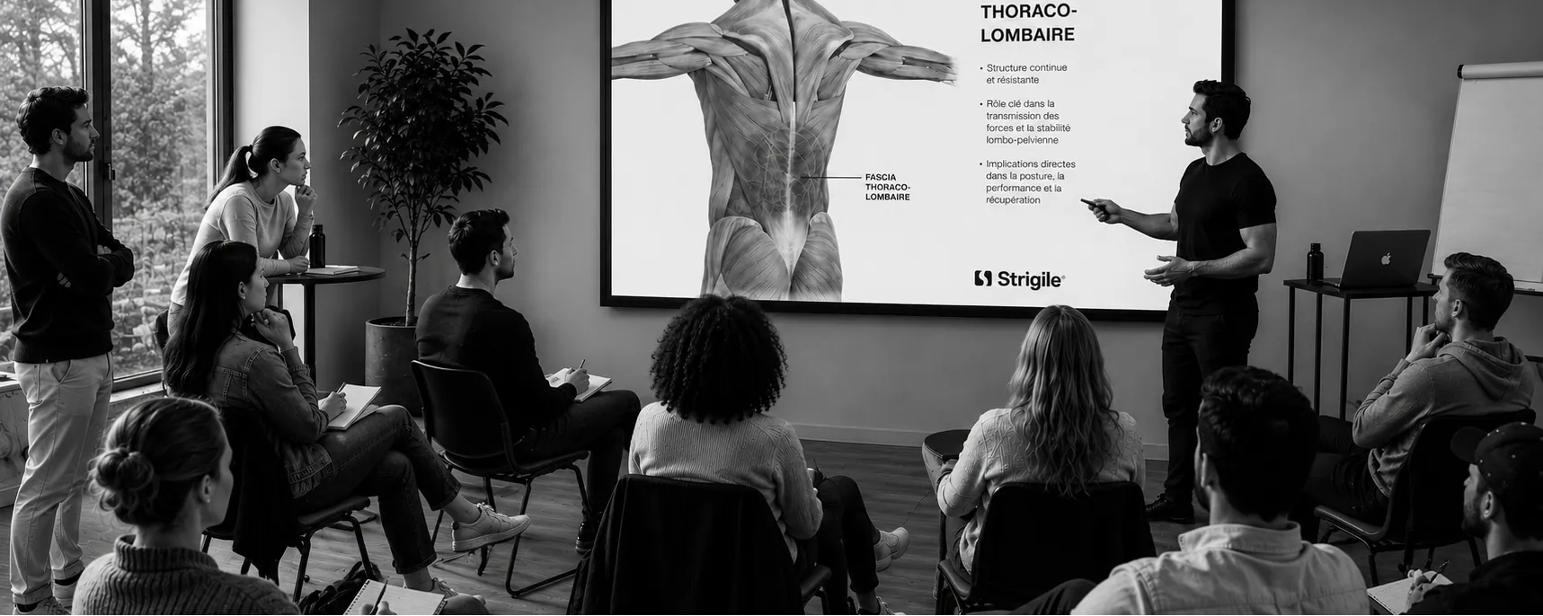 Salle de séminaire : un formateur commente une planche anatomique du fascia thoraco-lombaire devant les participants