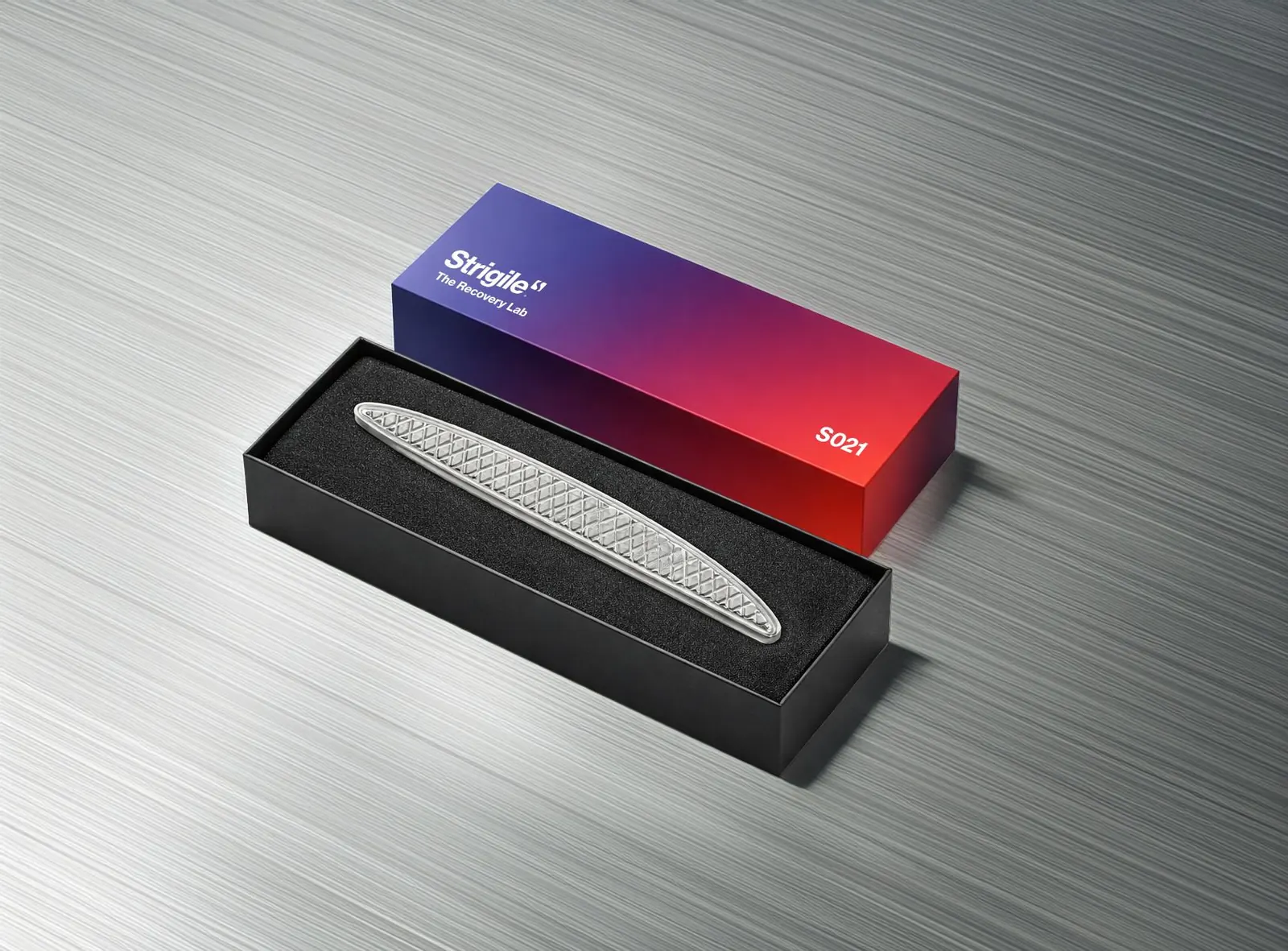 L’instrument STRIGILE en acier poli, posé dans son coffret au dégradé de la marque